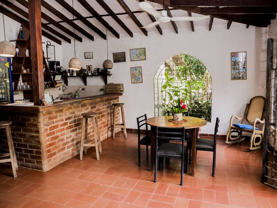 Una zona de bar rústica con mostrador de ladrillo, taburetes de madera y una mesa redonda con sillas.