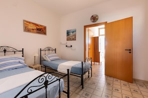 Une chambre avec deux lits, une porte en bois et un sol carrelé.