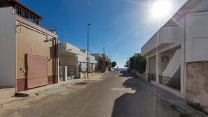 A quiet street with buildings on either side, a clear sky, and a sun shining.
