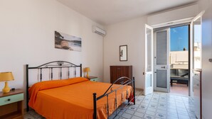 A bedroom with a bed, a nightstand, an air conditioner, a wooden cabinet, and a door leading to a balcony.