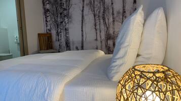 A bedroom with a bed, white bedding, a wall-mounted air conditioner, and a wall with a birch tree wallpaper.