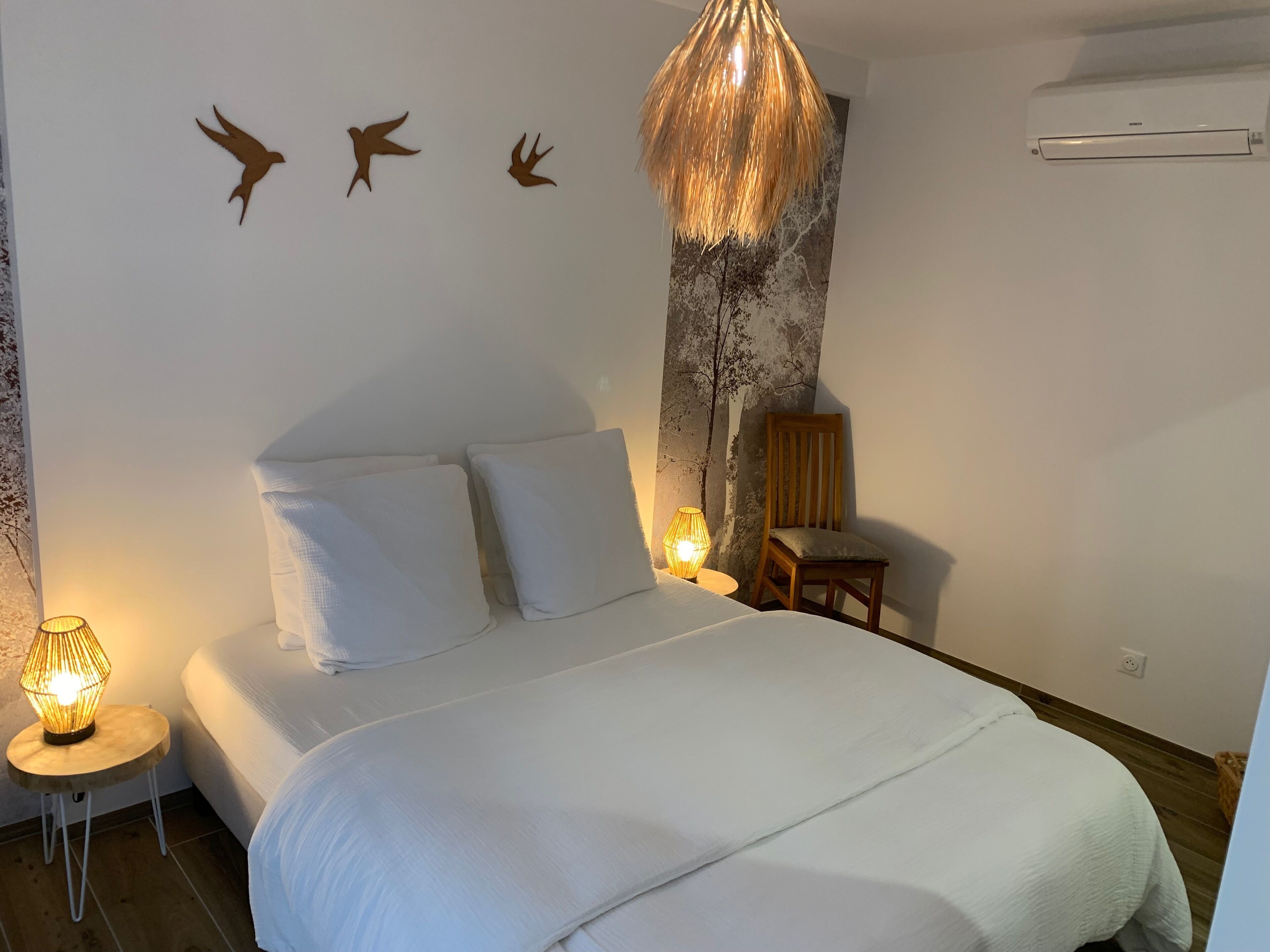 A bedroom with a bed, a nightstand, a lamp, a chair, and wall art.