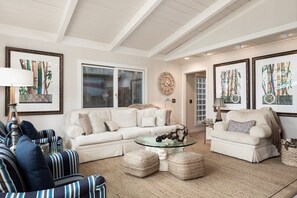 A spacious living room with a large beige sectional sofa, a glass coffee table, and a striped armchair.