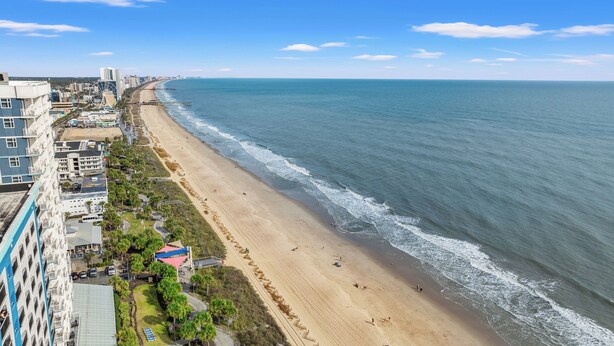 A coastal cityscape with a wide sandy beach, a pier, and high-rise buildings along the shore. - The Anchor Hotel (Myrtle Beach)