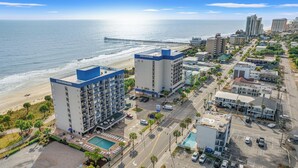 A beachfront hotel with multiple floors, a swimming pool, and a pier in the background. - The Anchor Hotel (Myrtle Beach)