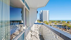 A balcony with white plastic chairs, a view of the ocean, and a tall building in the background. - The Anchor Hotel (Myrtle Beach)