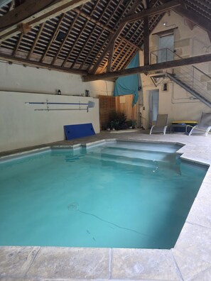 Une piscine intérieure dotée d’un sol carrelé et d’une structure de plafond en bois.