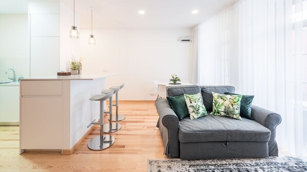 Un espace de vie moderne comprenant un canapé gris, un petit coin cuisine et un bar avec des tabourets.