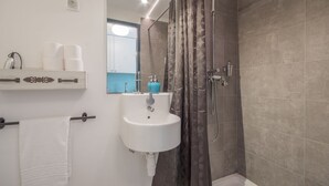 A bathroom with a white sink, a mirror, a shower with a curtain, and a towel rack. - Lisbon Heart Apartments - White, by LovelyStay (Lisboa)