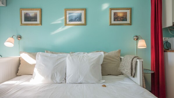 Un lit avec une literie blanche, des oreillers beige et une couverture. Trois tableaux encadrés sont accrochés au mur au-dessus du lit.