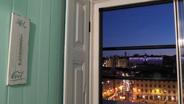 Blick auf eine Stadtlandschaft im Abendlicht durch ein Fenster, an der Wand hängt ein Thermometer.
