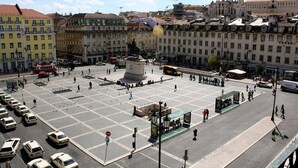 Ein Platz mit einem zentralen Denkmal, umgeben von Gebäuden und parkenden Autos.