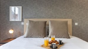 A neatly made bed with two pillows, a bedside table with a lamp, and a tray with breakfast including croissants, juice, and coffee cups.