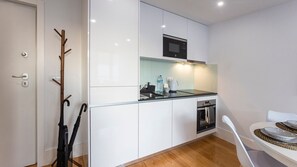 A compact kitchen with white cabinets, a microwave, a sink, and a small oven. There is a dining table with a woven placemat and a white chair.