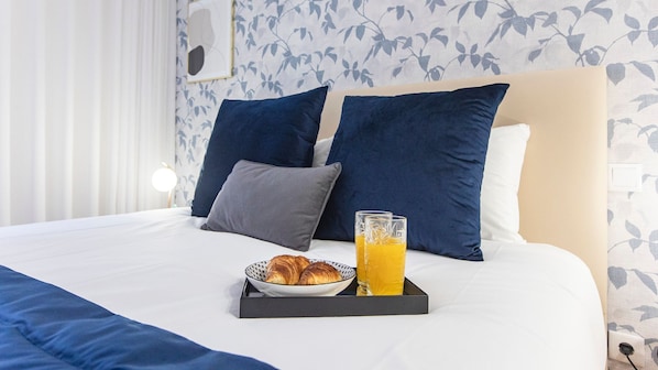 A neatly made bed with a tray of croissants and orange juice, a bedside lamp, and a floral wallpaper pattern.