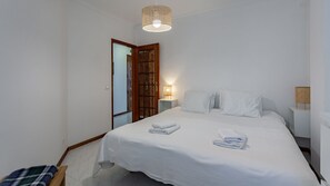 A bedroom with a bed, a nightstand, a lamp, a door, and a bench.