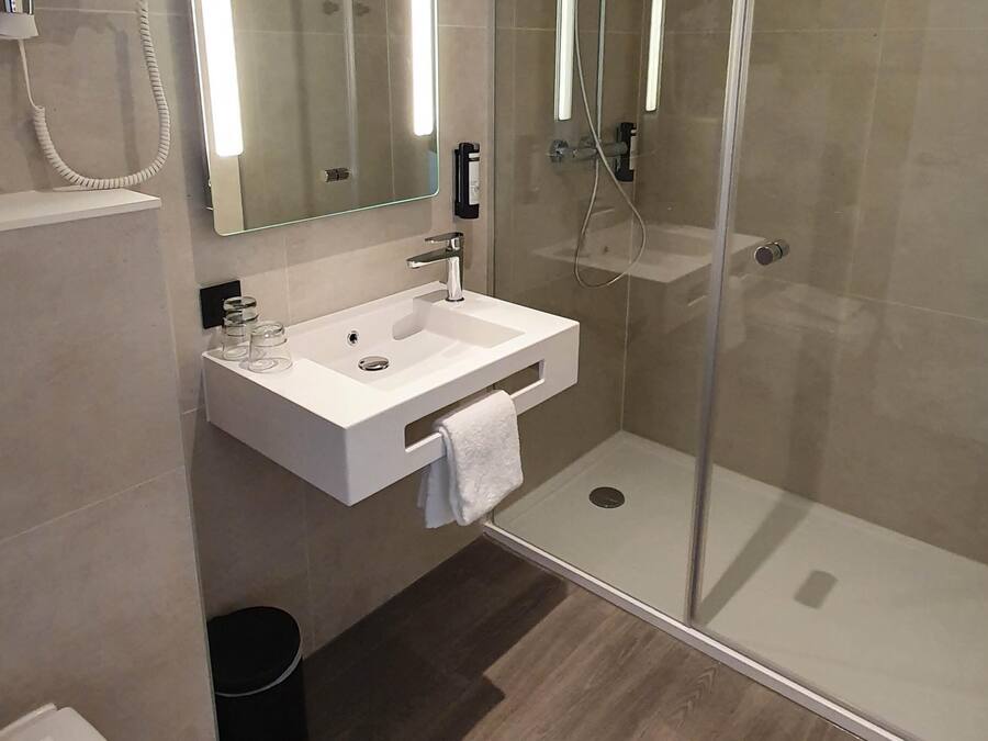 Een moderne badkamer met een douche met glazen wand, een witte wastafel en een spiegel erboven.