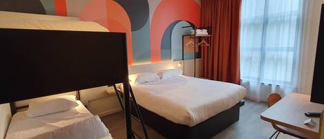 Habitación de hotel con cama, escritorio, silla, espejo y ventana con cortinas.