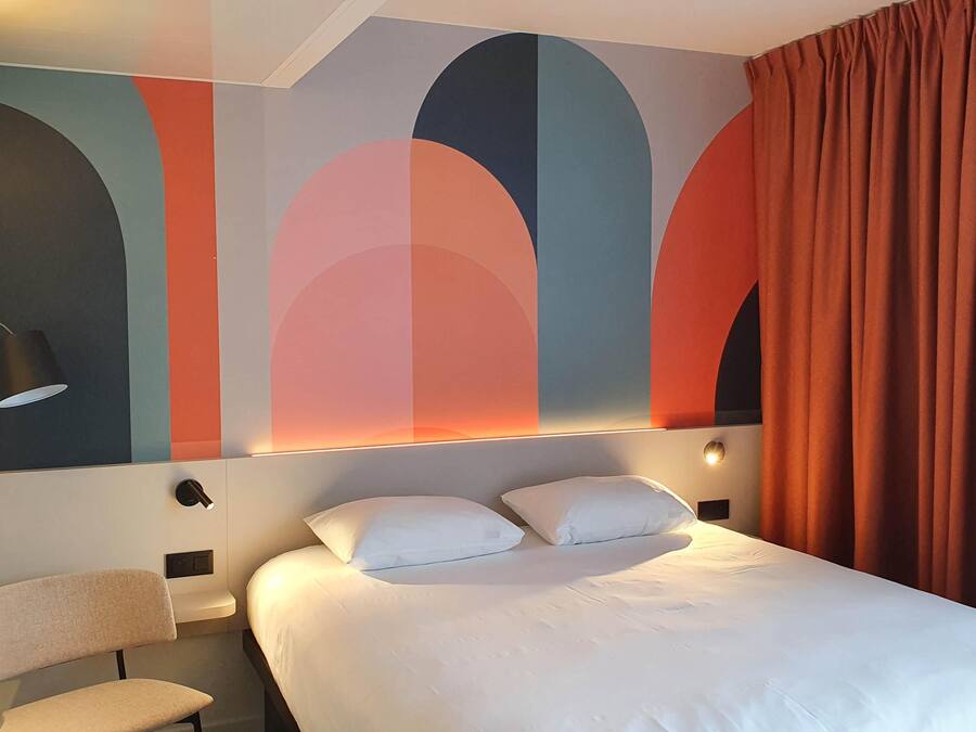 Habitación de hotel con cama, una silla, un muro con arte abstracto y una cortina.