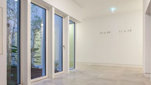 Un interior modern amb grans portes corredisses de vidre que donen a un jardí, una paret blanca i neta amb números de les habitacions, i un paviment de rajola.