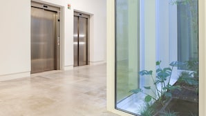 Passadís amb dos ascensors i una paret de vidre que ofereix vistes a un jardí.