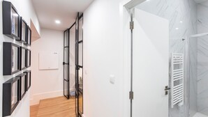 Un couloir moderne avec un plancher en bois, une porte blanche donnant sur une salle de bain équipée d’un porte-serviettes blanc et d’une cabine de douche en verre.