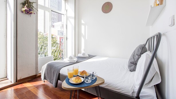 A hotel room with a bed, a small table with breakfast items, and a window with a view of buildings. - Bonjardim Studio w/ Balcony by LovelyStay (Porto)