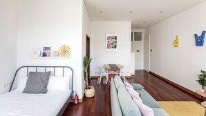 A modern, well-lit bedroom with a bed, bedside table, and a small desk. There is a sofa and a chair in the living area, and a door leading to another room. - Bonjardim Studio w/ Balcony by LovelyStay (Porto)