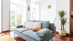 A modern living room with a grey sofa, a small potted plant, and a view of the outside. - Bonjardim Studio w/ Balcony by LovelyStay (Porto)