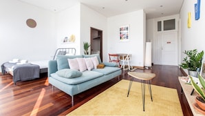A modern living room with a blue sofa, a small round table, and a bed with rolled towels. - Bonjardim Studio w/ Balcony by LovelyStay (Porto)