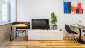 Una sala moderna con una televisión de pantalla plana, una mesa de comedor con sillas, una planta en maceta y un cuadro en la pared.