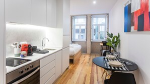 Cocina funcional con estufa, lavamanos y electrodomésticos modernos. Cuenta con un pequeño comedor con mesa y sillas, y una cama en una esquina.