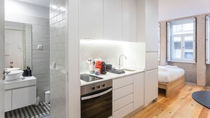Una habitación de hotel compacta con kitchenette, baño pequeño y cama con ventana.