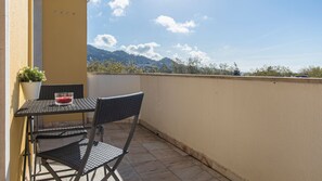 Un balcone con tavolo e due sedie, una pianta in vaso e un bicchiere di bevanda rossa.