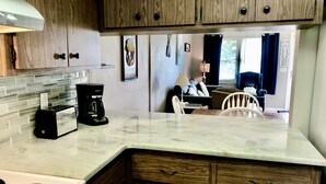 A kitchen with wooden cabinets, a marble countertop, a coffee maker, and a stove. - Melbourne Beach Beachfront, Oceanfront nearly secluded Beach Unit A (Melbourne Beach)