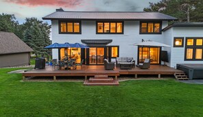 Ein zweistöckiges Haus mit einer Terrasse, Sitzgelegenheiten im Freien und einer überdachten Veranda.