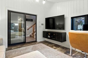 Een moderne woonkamer met een schuifdeur naar een trap, een flatscreen televisie bevestigd aan een donker houten dressoir, en een beige bank.