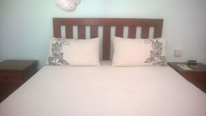 A bed with a wooden headboard, two pillows with floral designs, a bedside table with a 'No Smoking' sign, and a wall socket. - Gloria's Bed And Breakfast Accommodation (Livingstone)