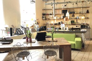 A cozy, well-lit cafe with a wooden table, metal chairs, and a green couch. - Canal-view Studio Sleeps 2 - Pets Welcome - Wifi (Schiedam)