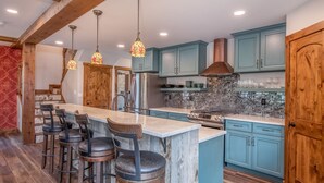 A kitchen with a marble island, bar stools, teal cabinets, and a stainless steel refrigerator. - New custom luxury home in historic downtown Crested Butte with hot tub & garage. (Crested Butte)