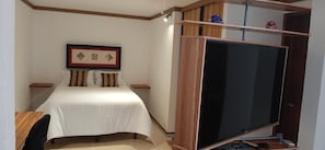 A bedroom with a bed, a TV, and a shelf with decorative items.
