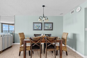 A dining area with a wooden table, wicker chairs, and two framed paintings on the wall. - Beachfront 3Br 2 Bath, Sleeps 8 Comfortably - Spectacular View (Orange Beach)
