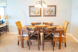 A dining area with a wooden table and chairs, two framed paintings on the wall, and a chandelier above.