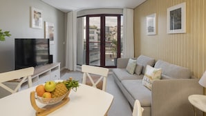 Een moderne woonkamer met een televisie, een eettafel met fruit, een bank en een uitzicht door een glazen deur naar buiten.