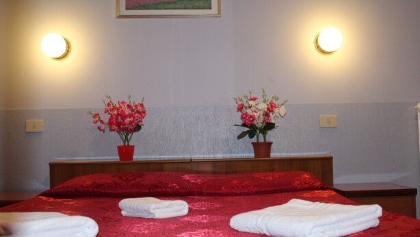 A hotel room with a red bedspread, two potted plants, and two wall-mounted lights. - Double Room (Roma)