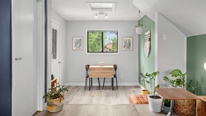 A hallway with a wooden table and chairs, a window with a view of greenery, and several potted plants. - Scarlet Manor | Mid Century Zen Suite. 1 BR. Near DT, C-train. (Calgary)