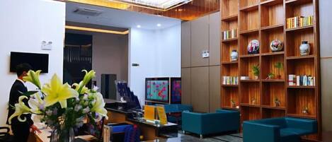 A hotel lobby with a reception desk, seating area, and a bookshelf.