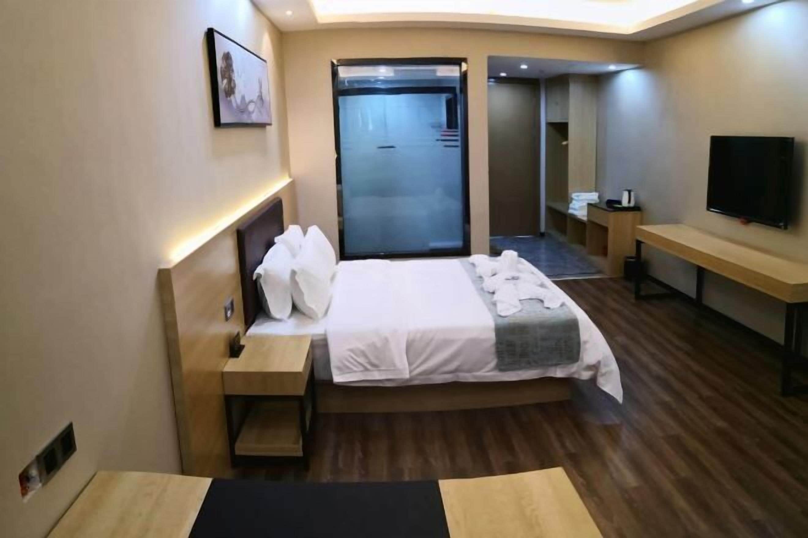 A hotel room with a bed, bedside tables, a TV, and a mirror.