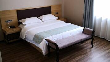 A hotel room with a wooden bed, a bench, a nightstand with a phone, and a window with curtains.