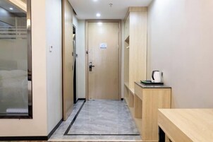 A hallway with a wooden door, a small table with a kettle, and a tiled floor.